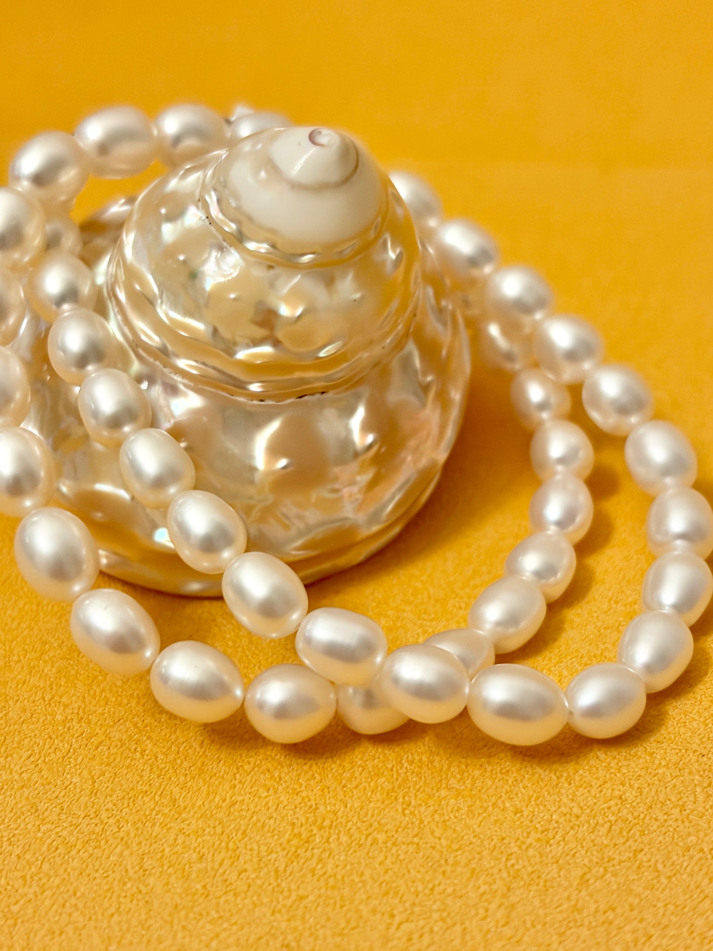 Pearl necklace draped over a clear glass bottle on a yellow background