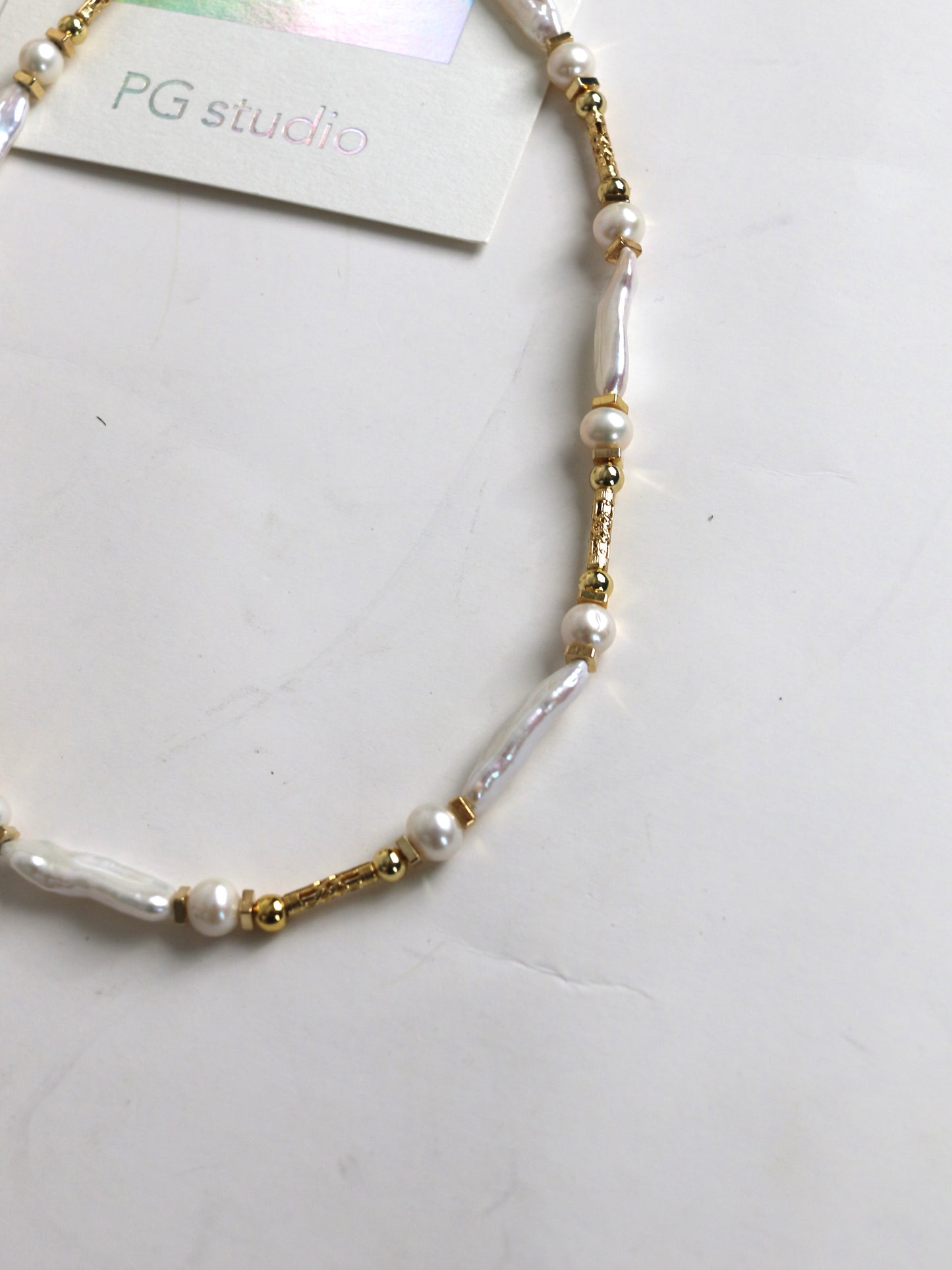 Pearl and gold beaded necklace for men on a white surface with 'PG studio' label.