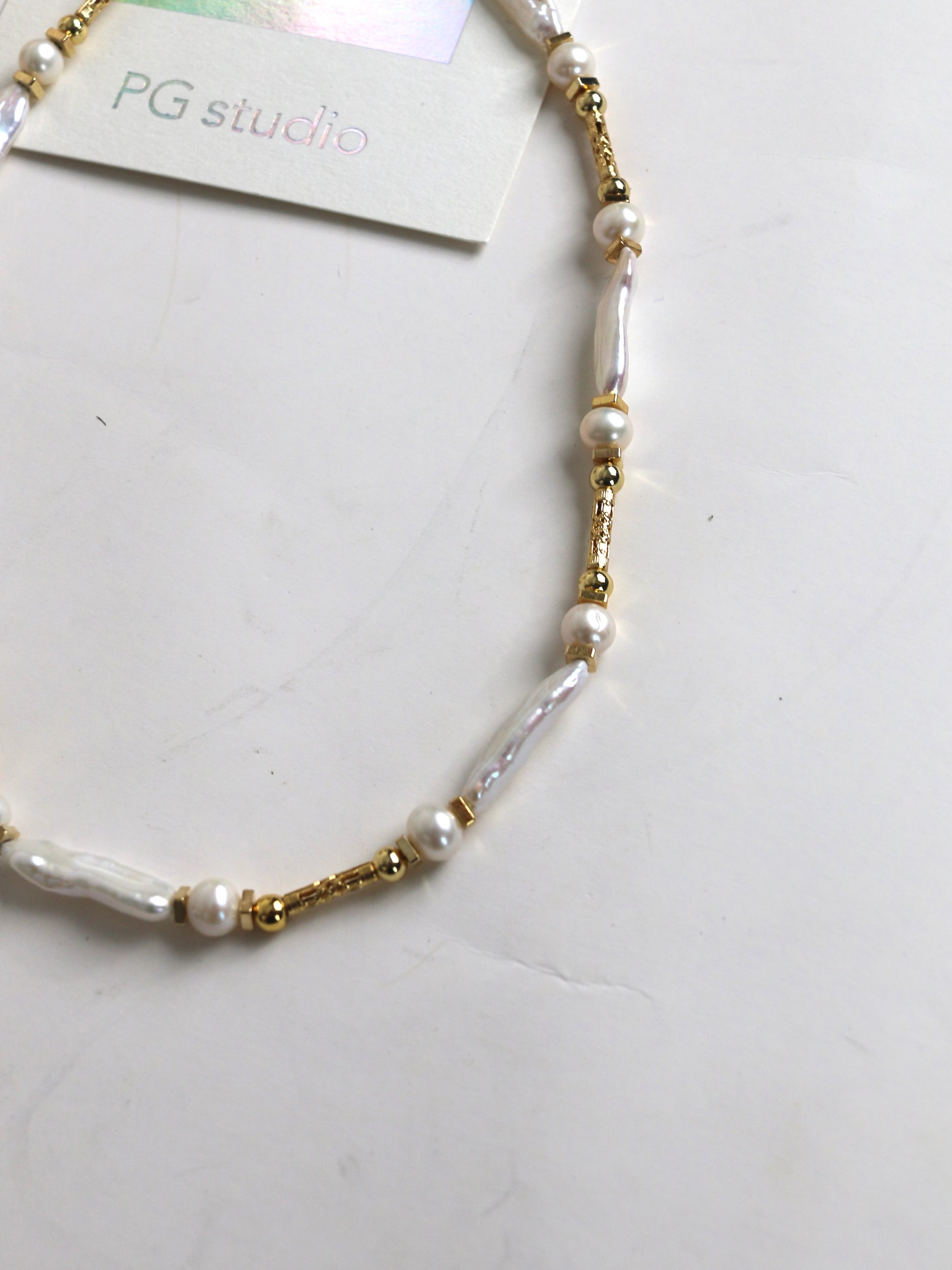 Pearl and gold beaded necklace for men on a white surface with 'PG studio' label.