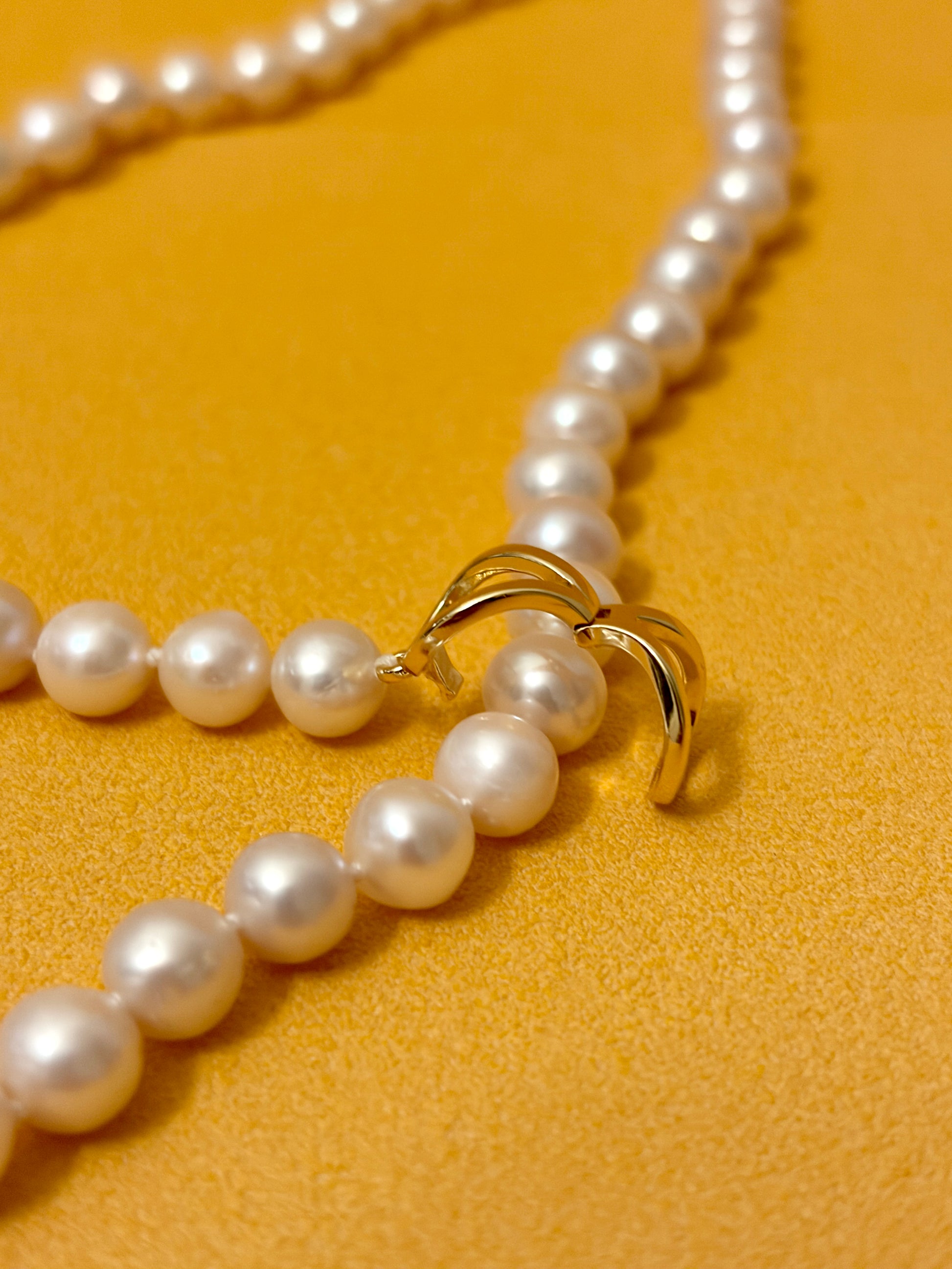 Close-up of the clasp on a White Round Freshwater Pearl Lariat Necklace on a vibrant yellow background.