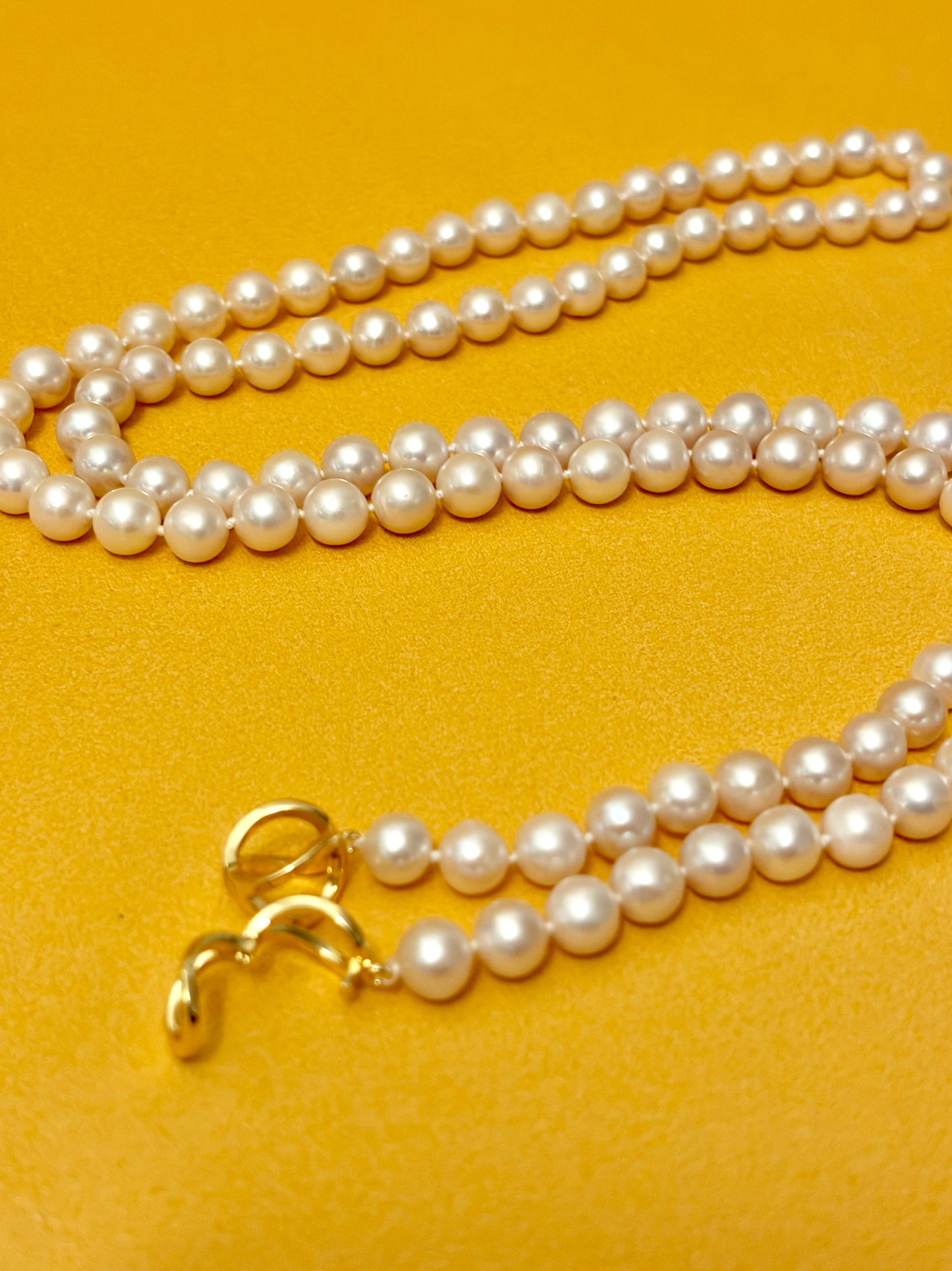 Pearl necklace with a gold clasp on a yellow background