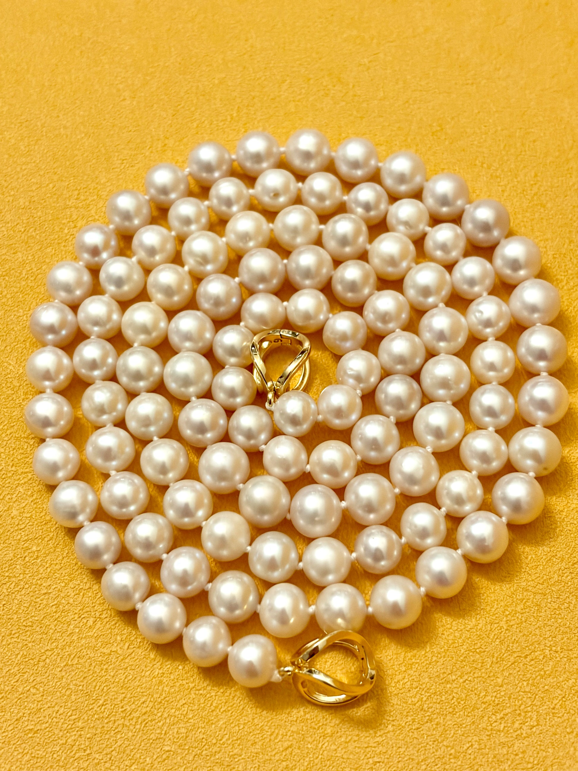 Pearl necklace with gold clasp on a yellow background