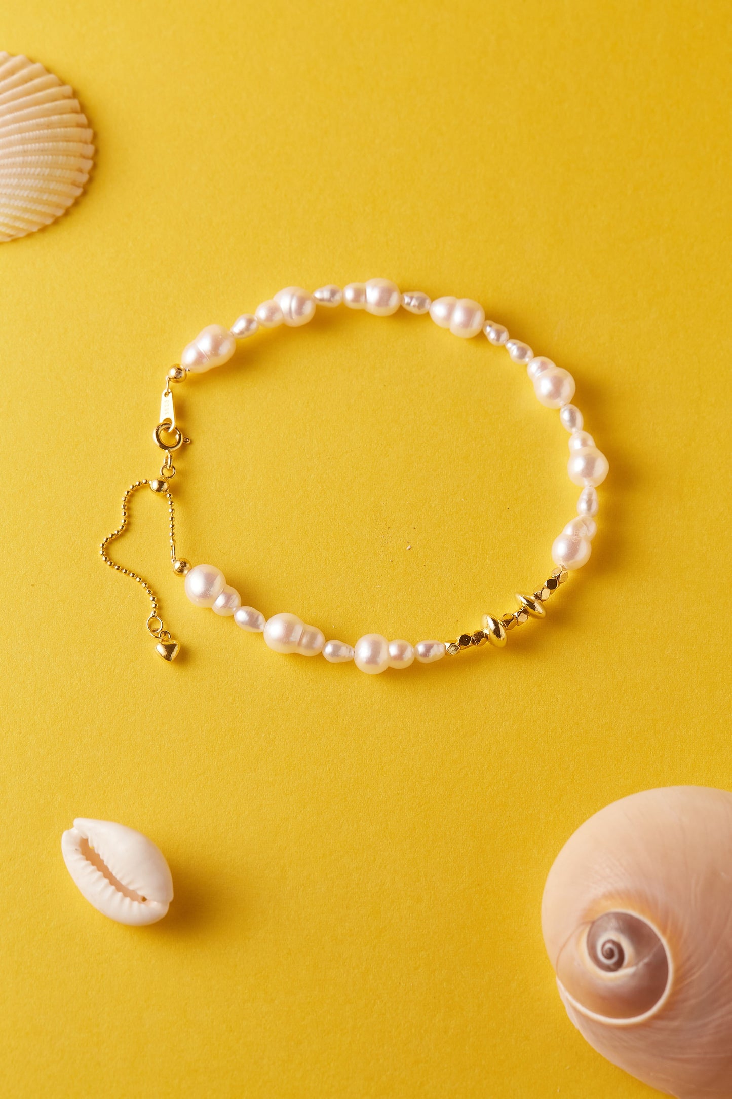Pearl bracelet with gold accents on a yellow background with shells