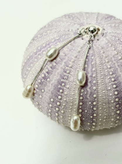 White Freshwater Pearl Chandelier Earrings displayed on a purple sea urchin shell, showcasing the elegant design.