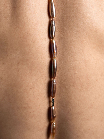 Close-up of a necklace with pearls on a person's neck against a neutral background