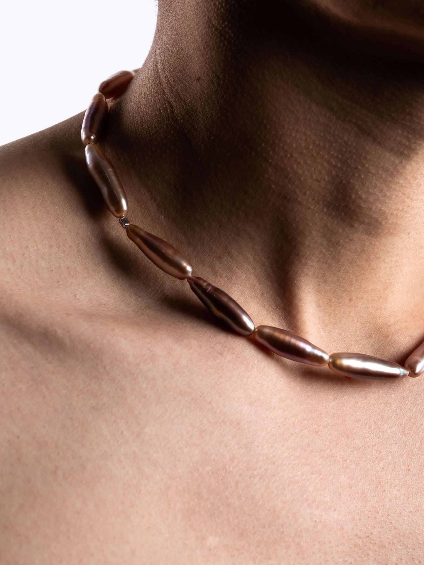 Pearl Necklace with brown beads on a person's neck against a neutral background