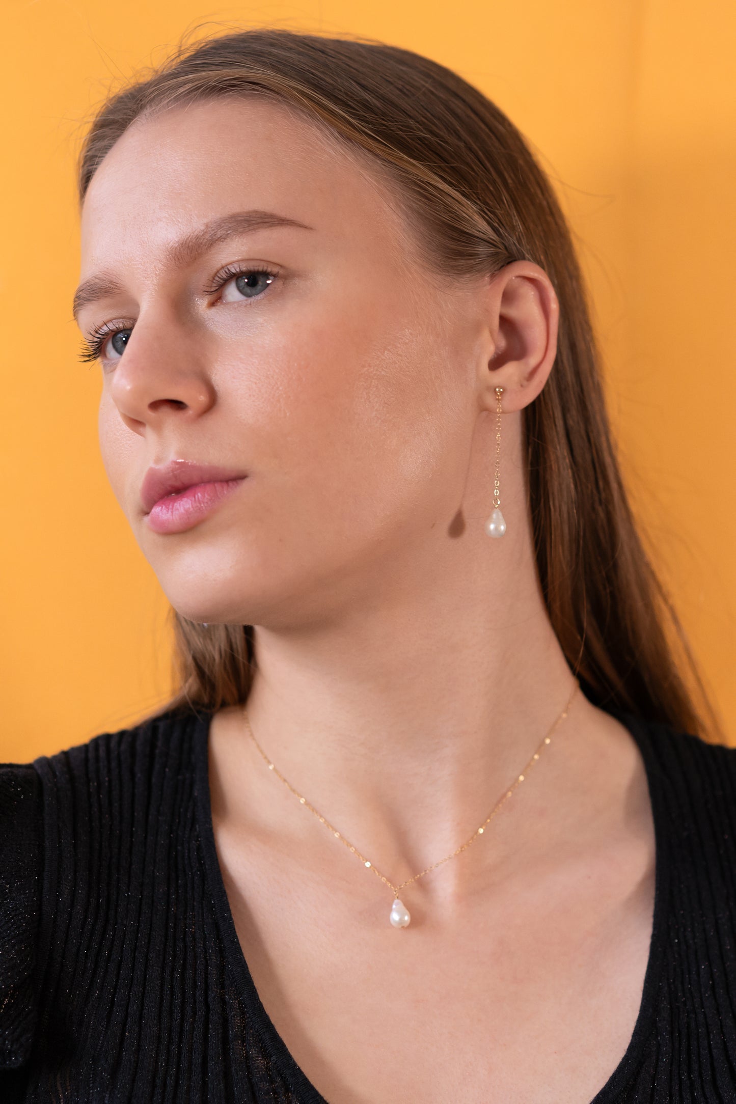 Woman wearing a pearl pendant necklace and earrings against an orange background