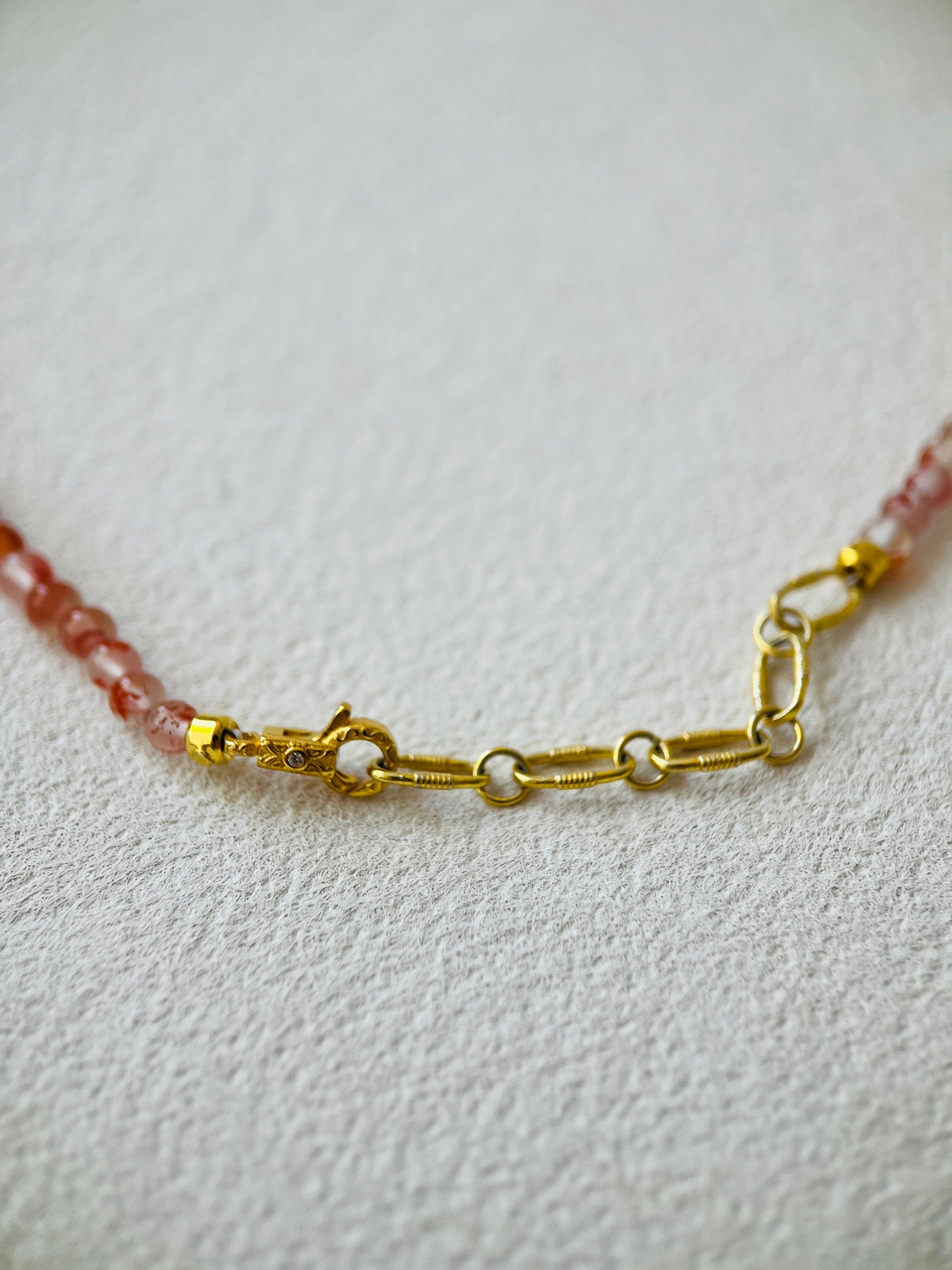 Golden clasp of pearl necklace with red carnelian gemstones on white background 