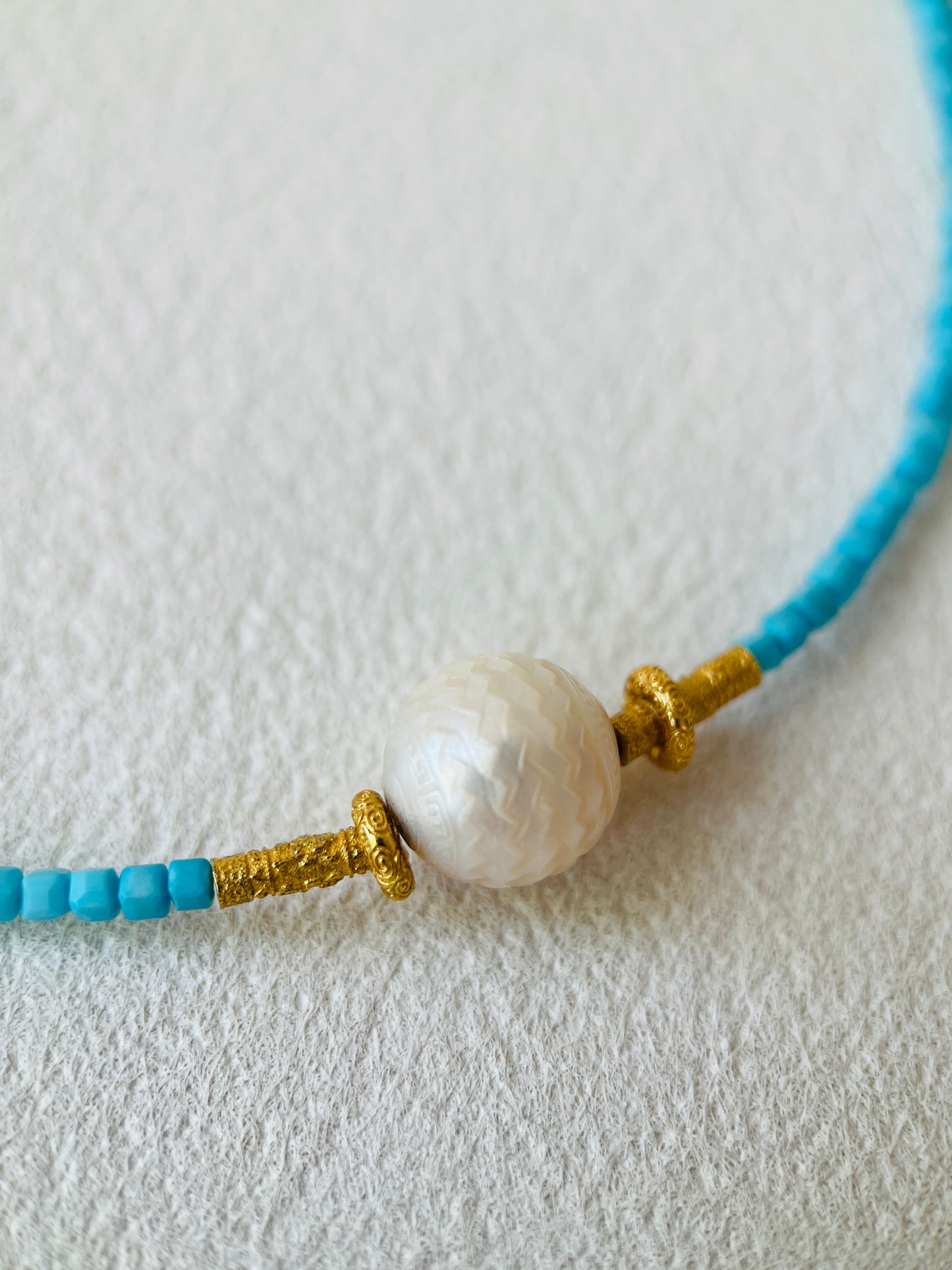 Close-up of a necklace with blue beads and a pearl and gold accent on a light gray background