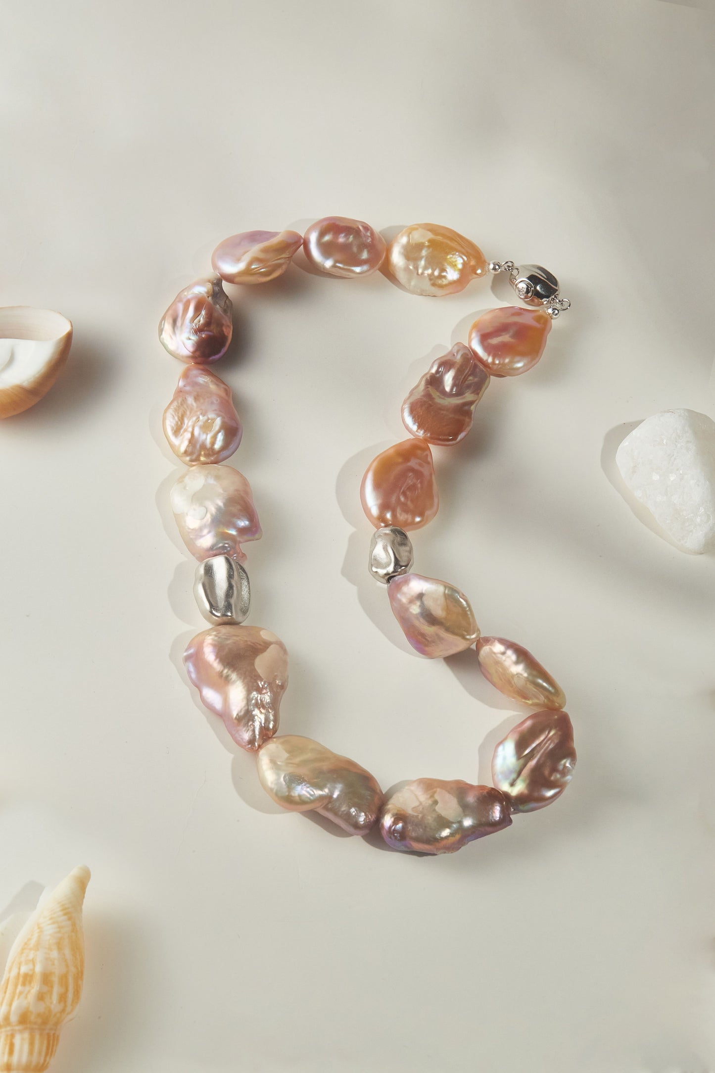 Necklace made of peach baroque pearls beads on a light background with shells.