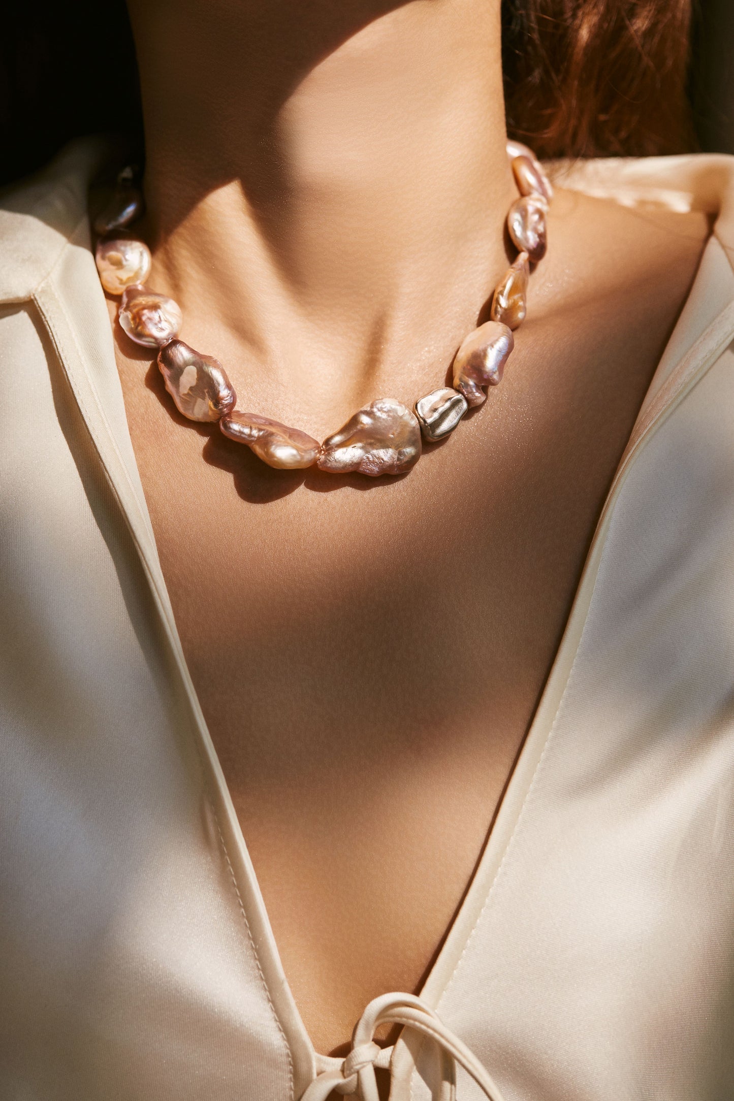 Necklace with peach baroque pearls worn by a person in a white outfit.